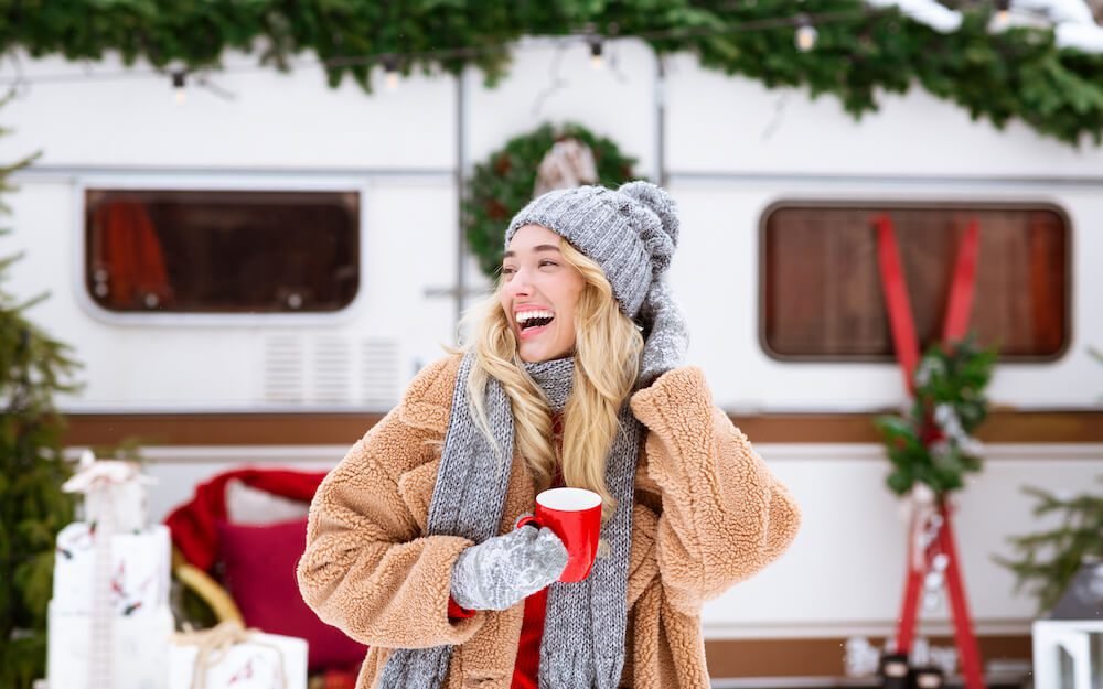 Winter Camping. Happy laughing female enjoying cup of tea near campervan outdoors